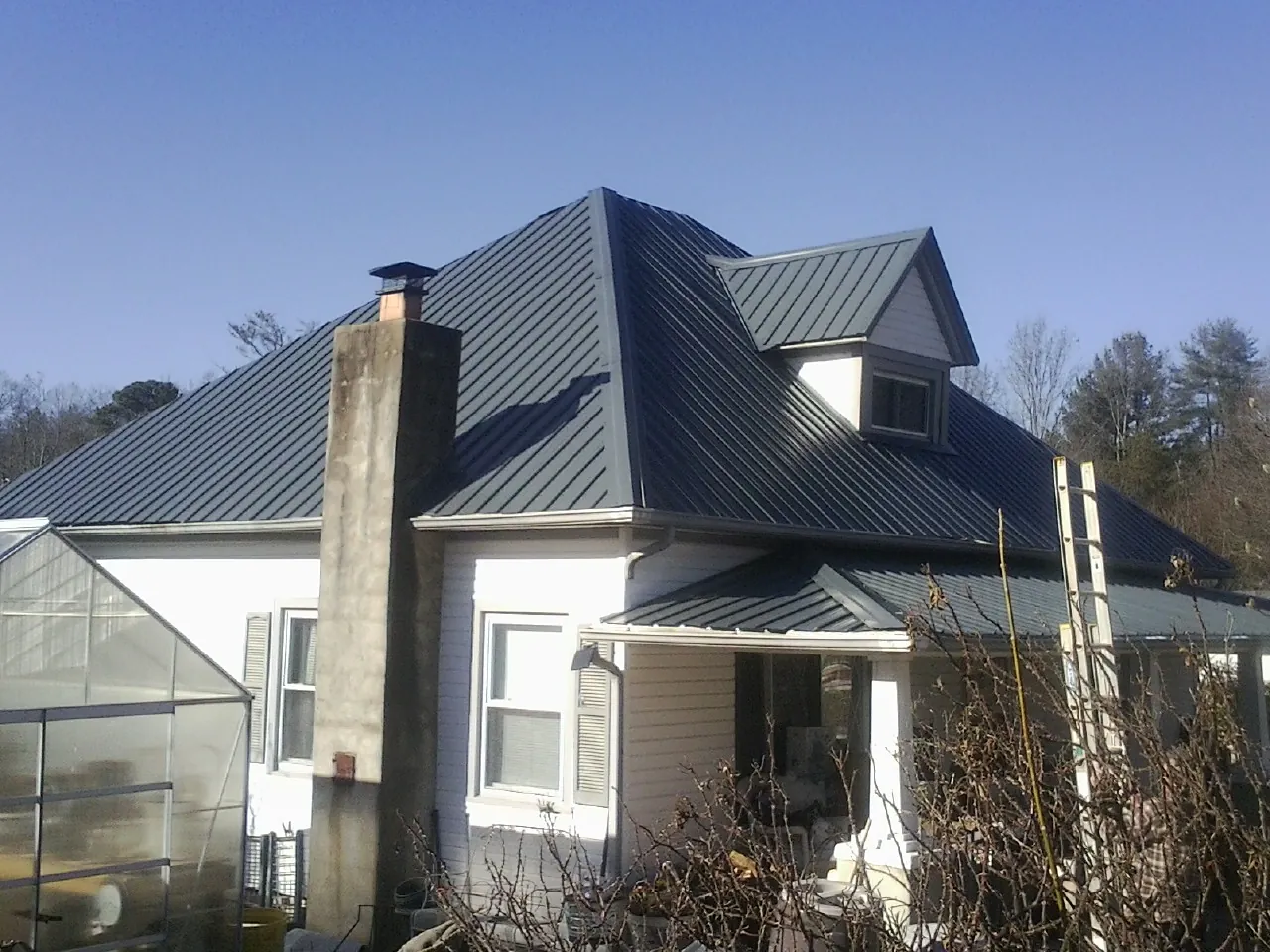 Dark blue standing seam metal roof on a white farmhouse with dormer — Slate & Tile Roof Repair by Roofing Brothers in Brighton
