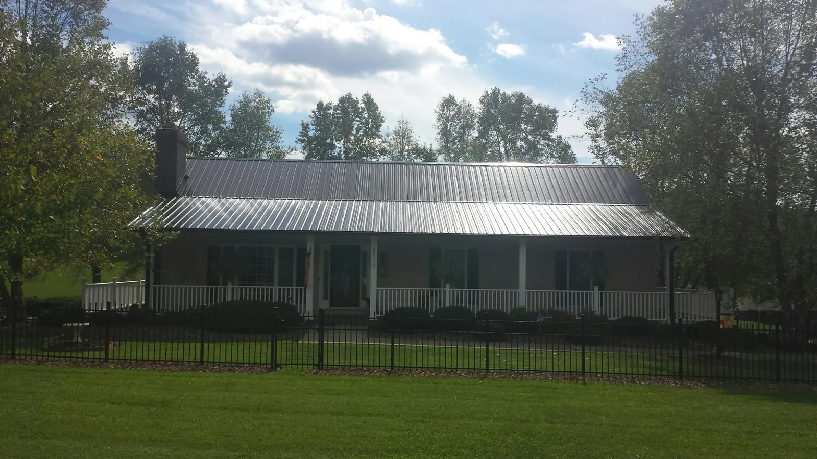 Gray metal roof on a brick ranch with a full width front porch — Gutter Guard Installation work by our crew in Brighton